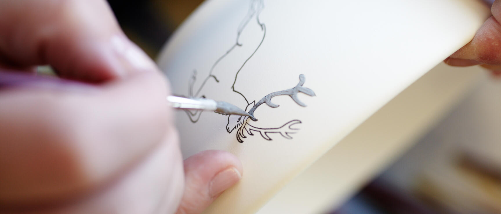 Close-up: Hand painting a ceramic object with a deer motif using a fine brush.