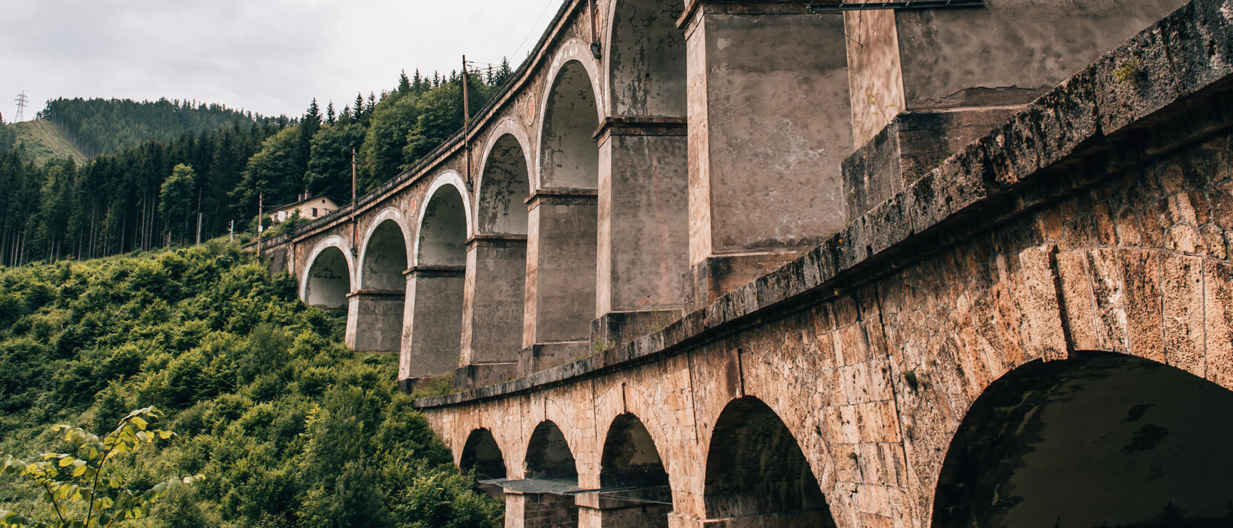 Stone railway viaduct with rounded arches winding through forested hills, Semmering Railway.