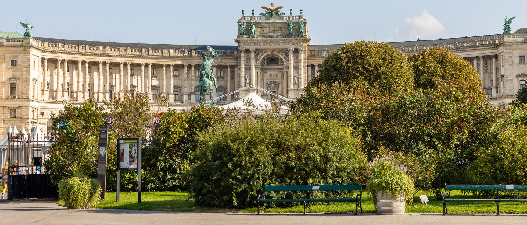 Neue Burg of Vienna Hofburg with equestrian statue, park with benches and trees in foreground.