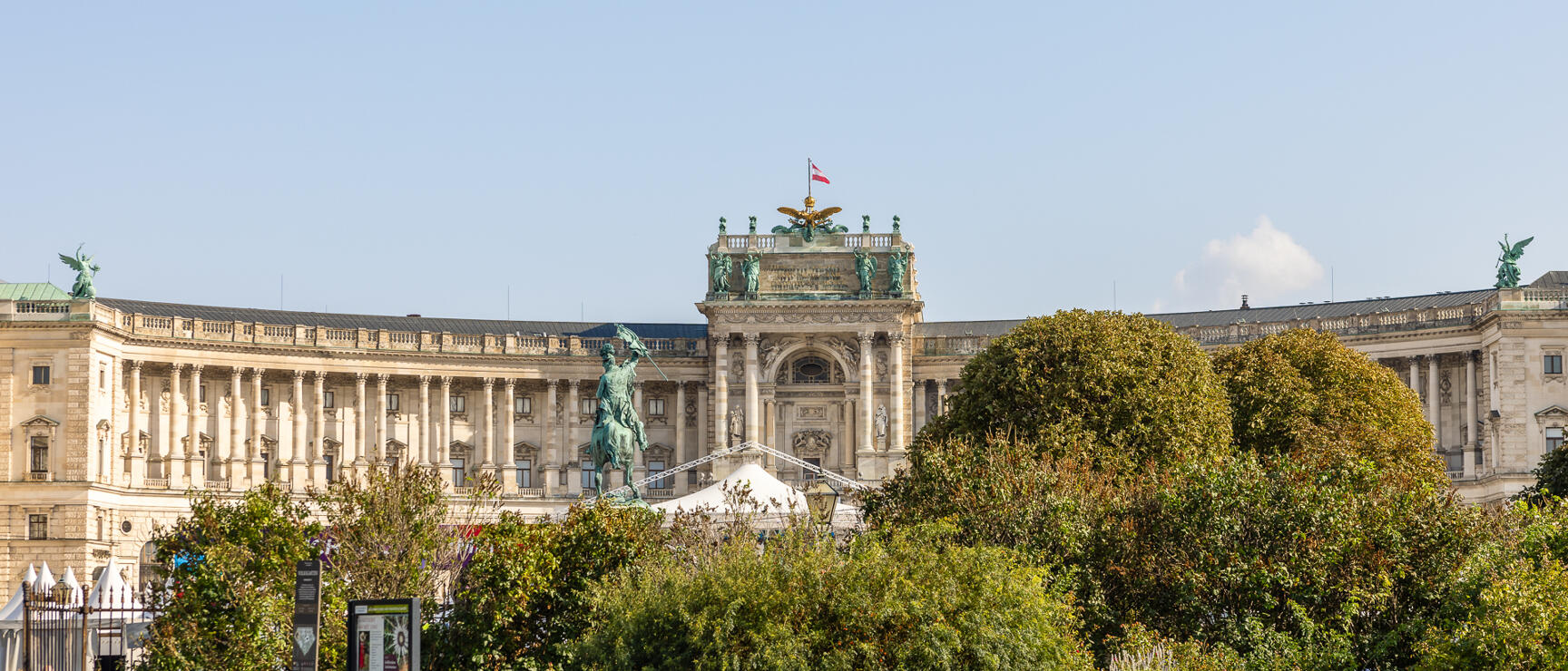 Neue Burg of Vienna Hofburg with equestrian statue, park with benches and trees in foreground.