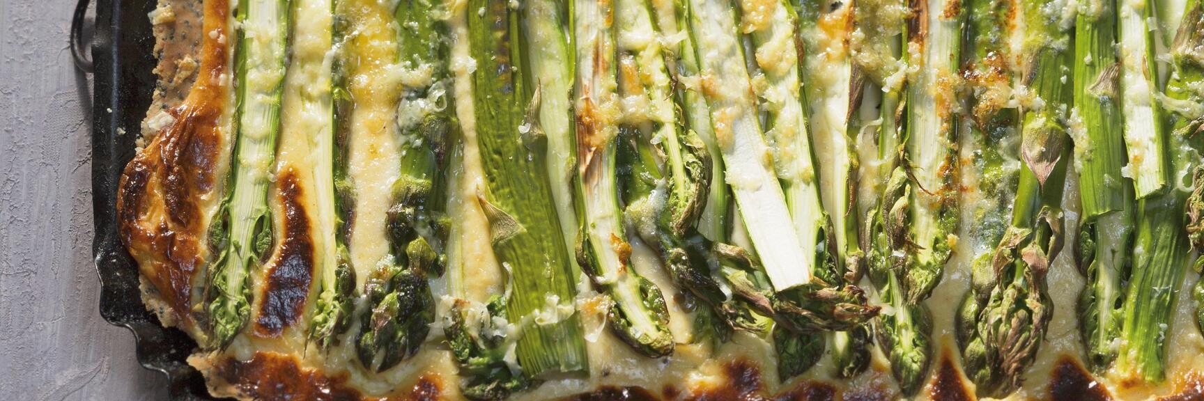 Gebackene Spargel-Quiche in eckiger Form, daneben altes Messer auf grauem Untergrund.