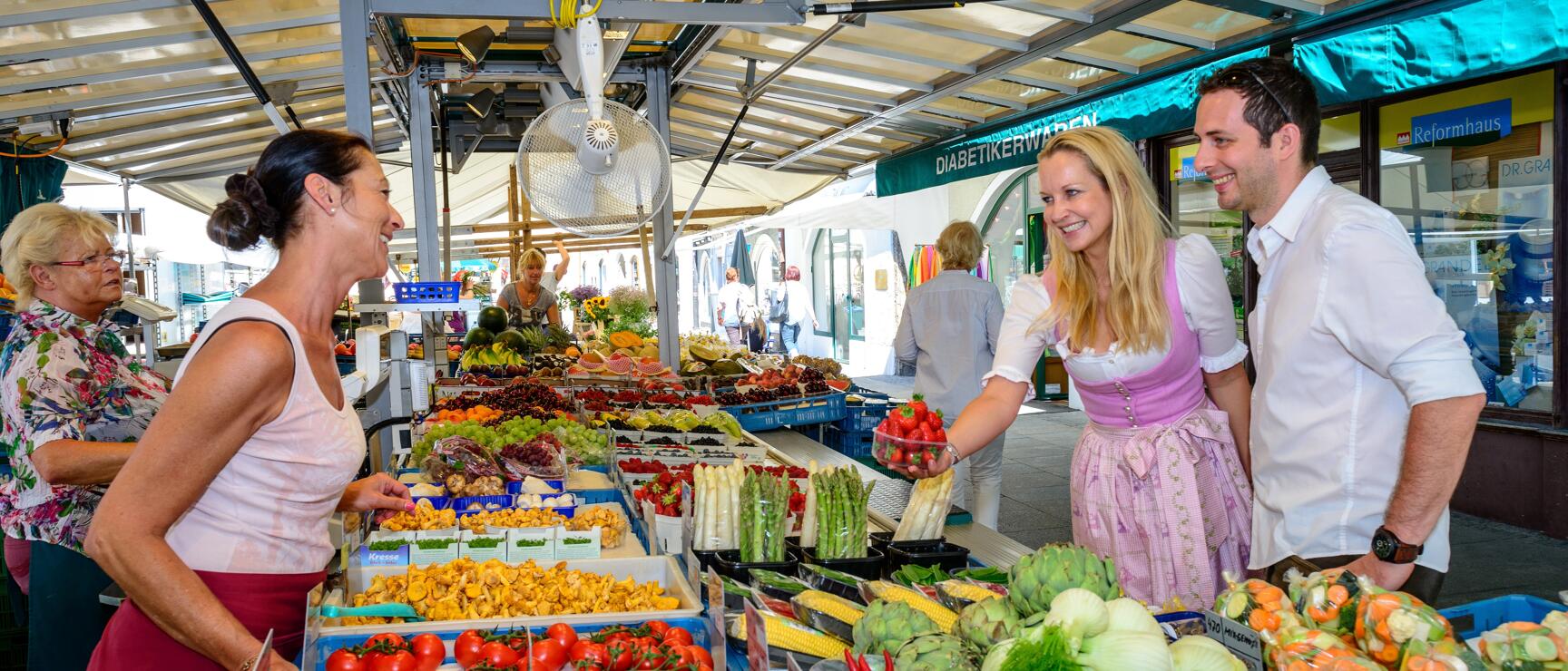 Couple in traditional dirndl and white shirt buying strawberries at a vegetable stand at a weekly market