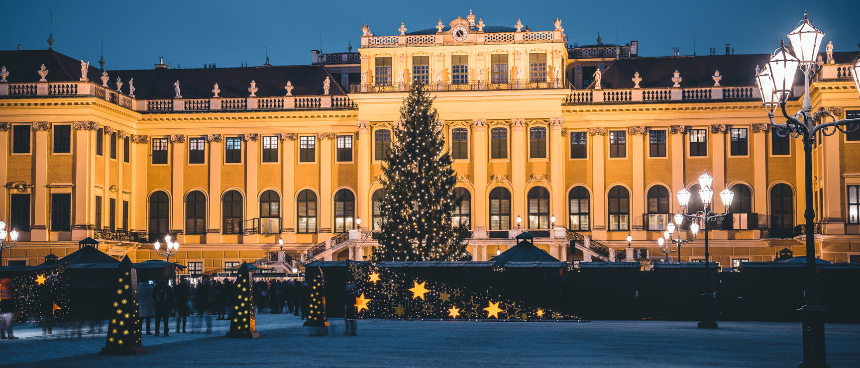 Christkindl market in front of Schönbrunn Palace at night, illuminated Christmas tree, yellow star decorations, Vienna.