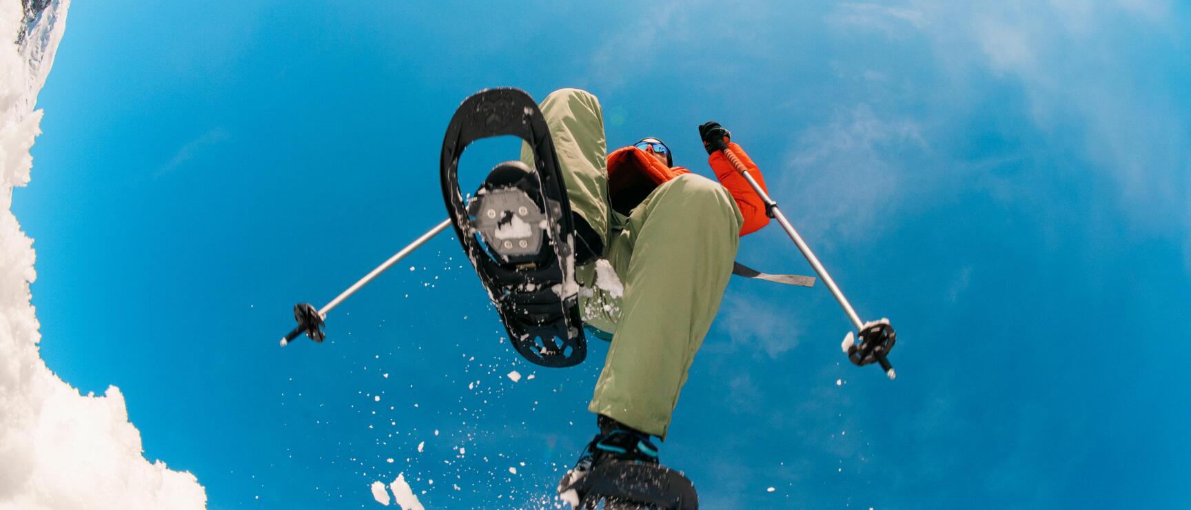 A person wearing snowshoes strides energetically through the snow-covered winter landscape. The low-angle view, the clear sky, and the swirling snow convey a sense of energy, a spirit of adventure, and the feeling of boundless freedom in the Austrian mountains.
