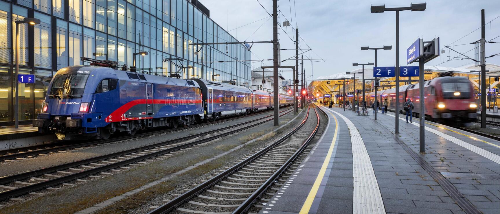 ÖBB Nightjet at platform 1, red train on track 3, glass façade in the background, dusk.