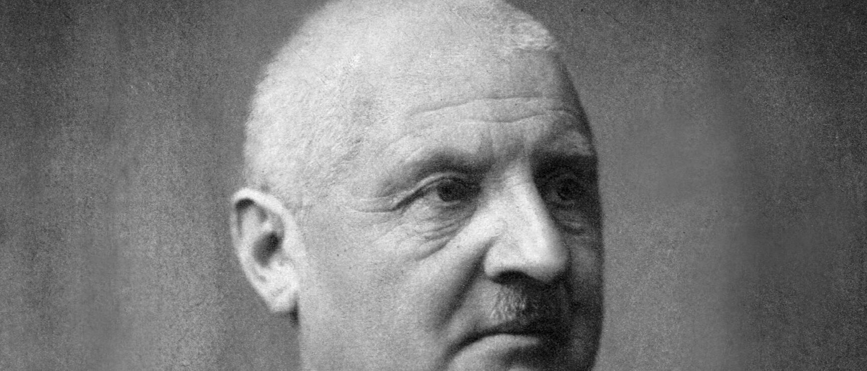 Historisches Schwarzweißporträt eines älteren Mannes mit Schnurrbart, dunklem Jackett und Krawatte.