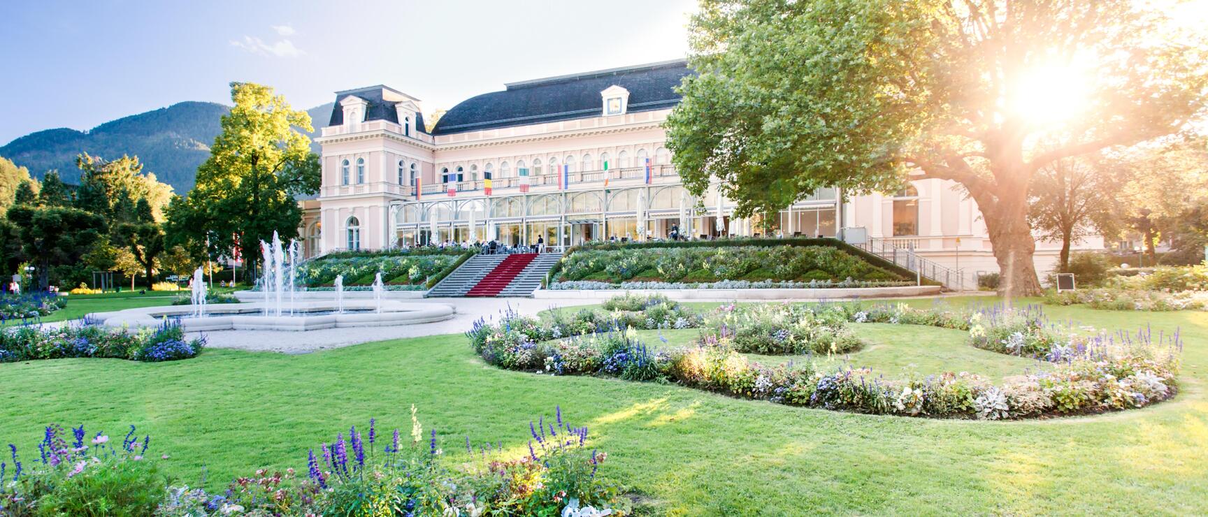 Historic spa house with flower beds, fountain and red staircase, mountain in background, Bad Ischl.