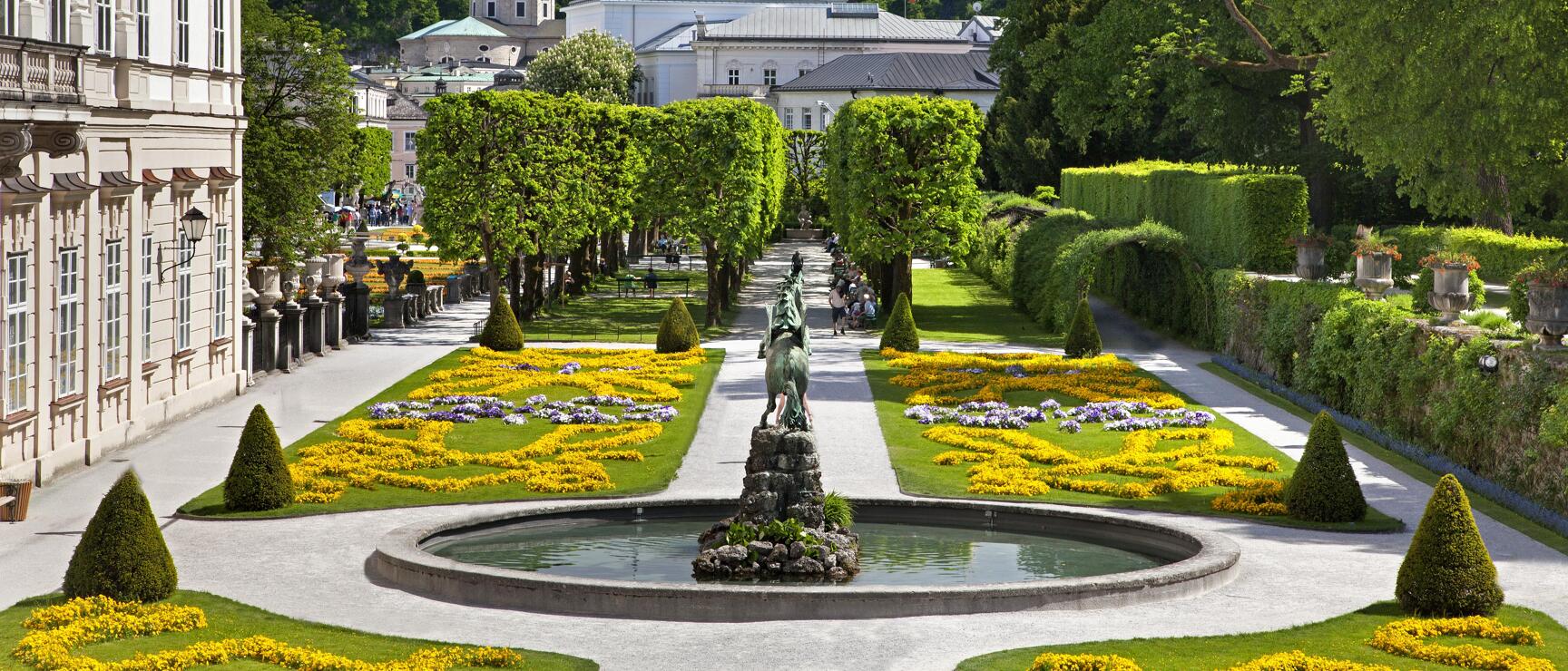 Mirabell Garden Salzburg with fountain, yellow flower beds, cathedral and Hohensalzburg Fortress in background.