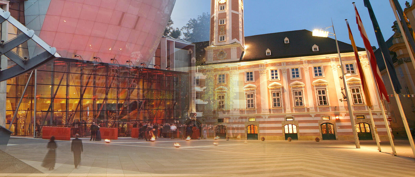 Illuminated town hall with clock tower and modern glass dome at St. Pölten town square at dusk.