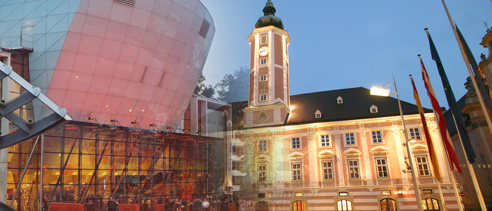 Illuminated town hall with clock tower and modern glass dome at St. Pölten town square at dusk.