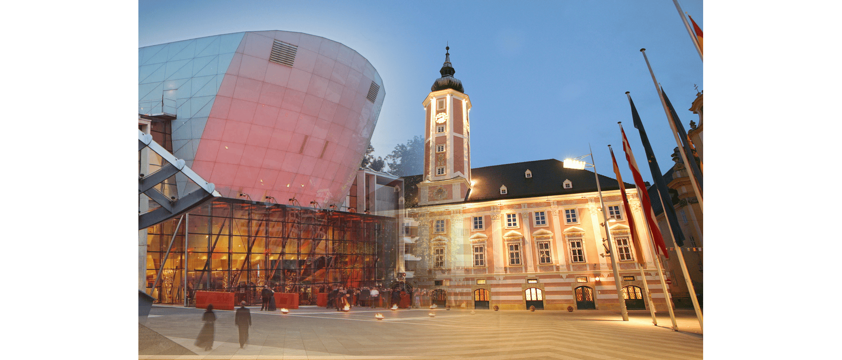 Illuminated town hall with clock tower and modern glass dome at St. Pölten town square at dusk.