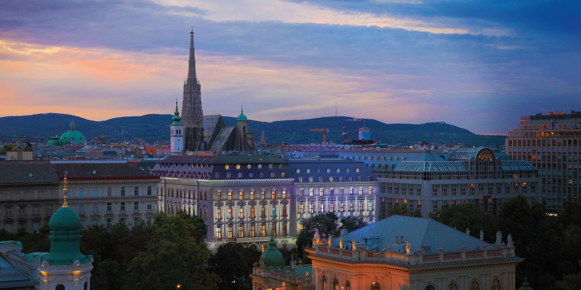Vienna city centre at dusk with St Stephen's Cathedral, illuminated Gründerzeit facades and hills in the background.