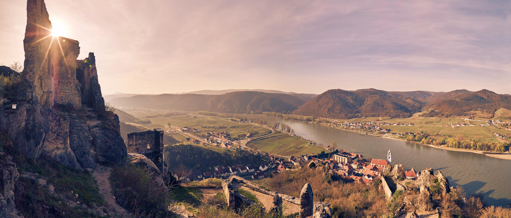 Ruine Dürnstein mit Blick auf Donau, Ortschaft und Weinberge in der Wachau bei Gegenlicht.