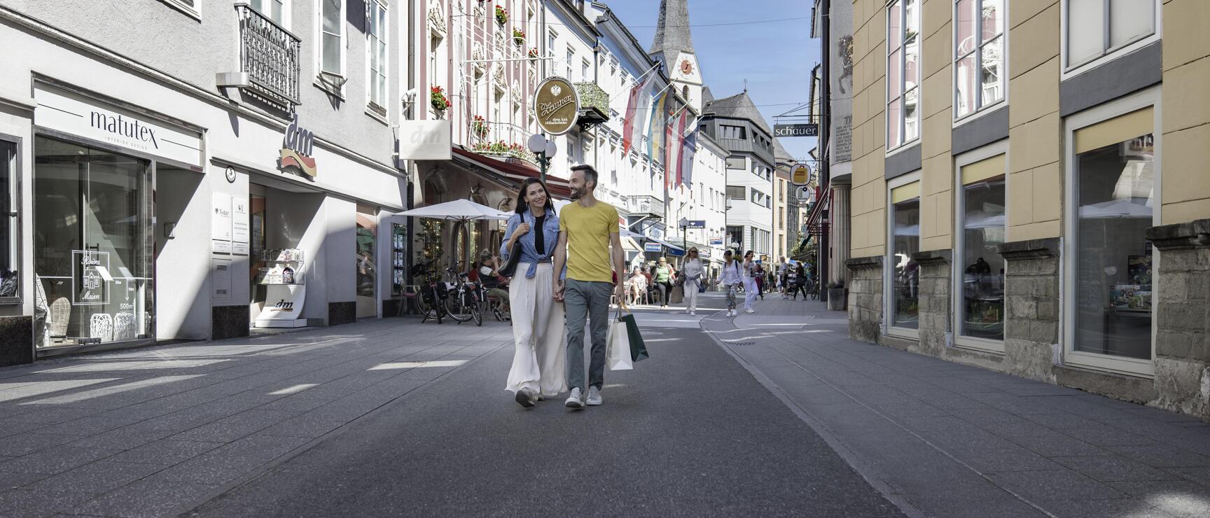 Couple with shopping bags in a pedestrian zone with shops and church tower in the background.