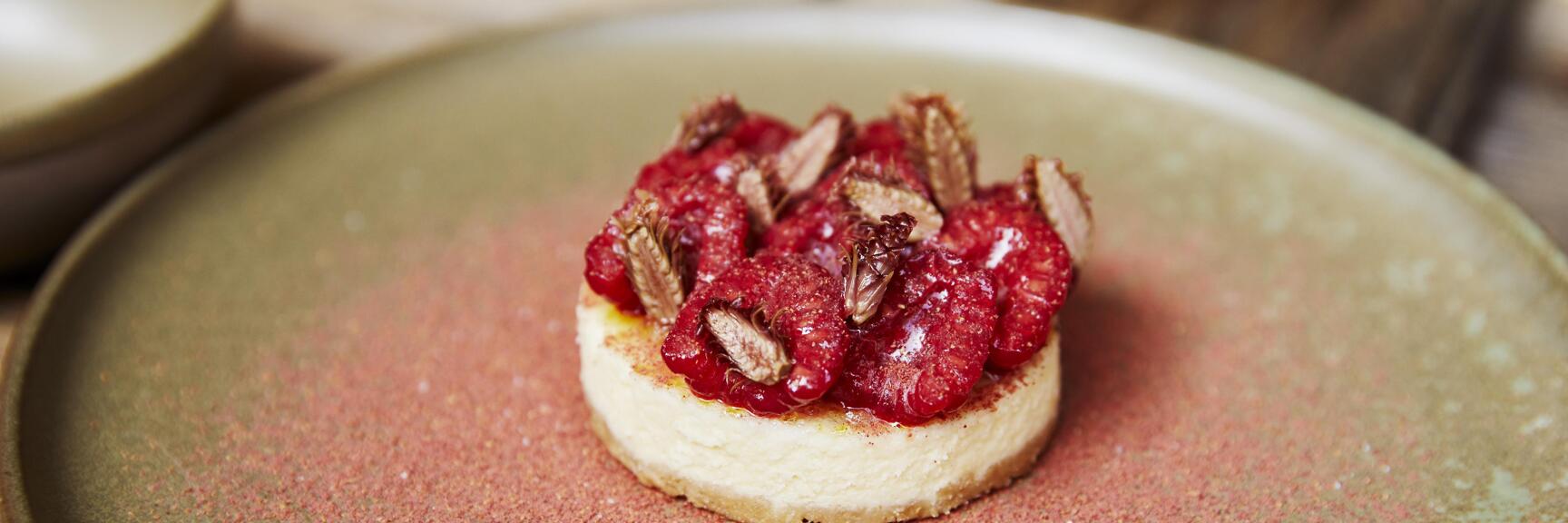 Small tart with raspberries and nuts on green ceramic plate, sprinkled with red powder.