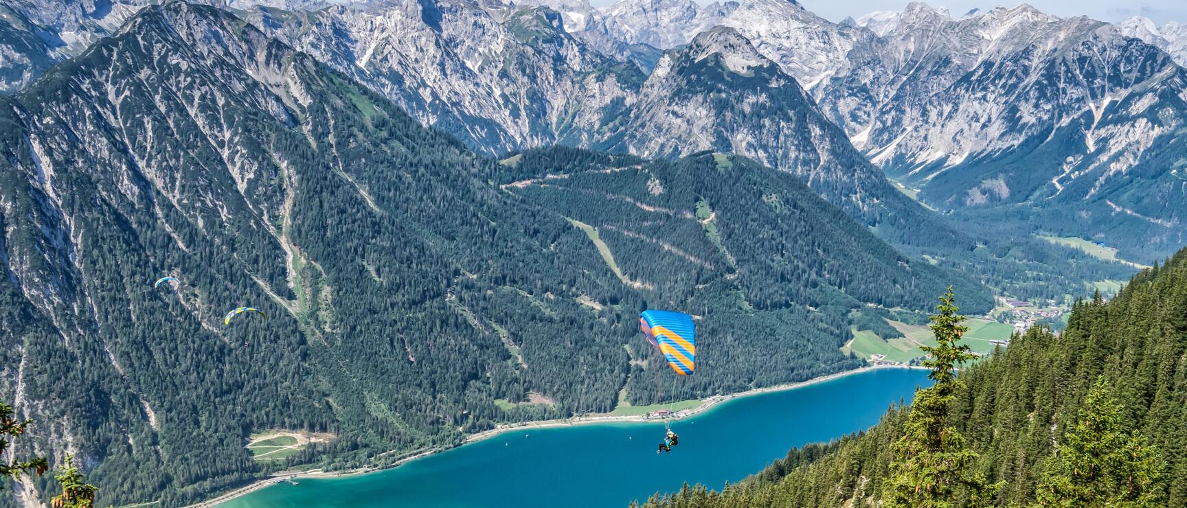 Paraglider over Lake Achensee in Tyrol, turquoise water, Karwendel Mountains in background.