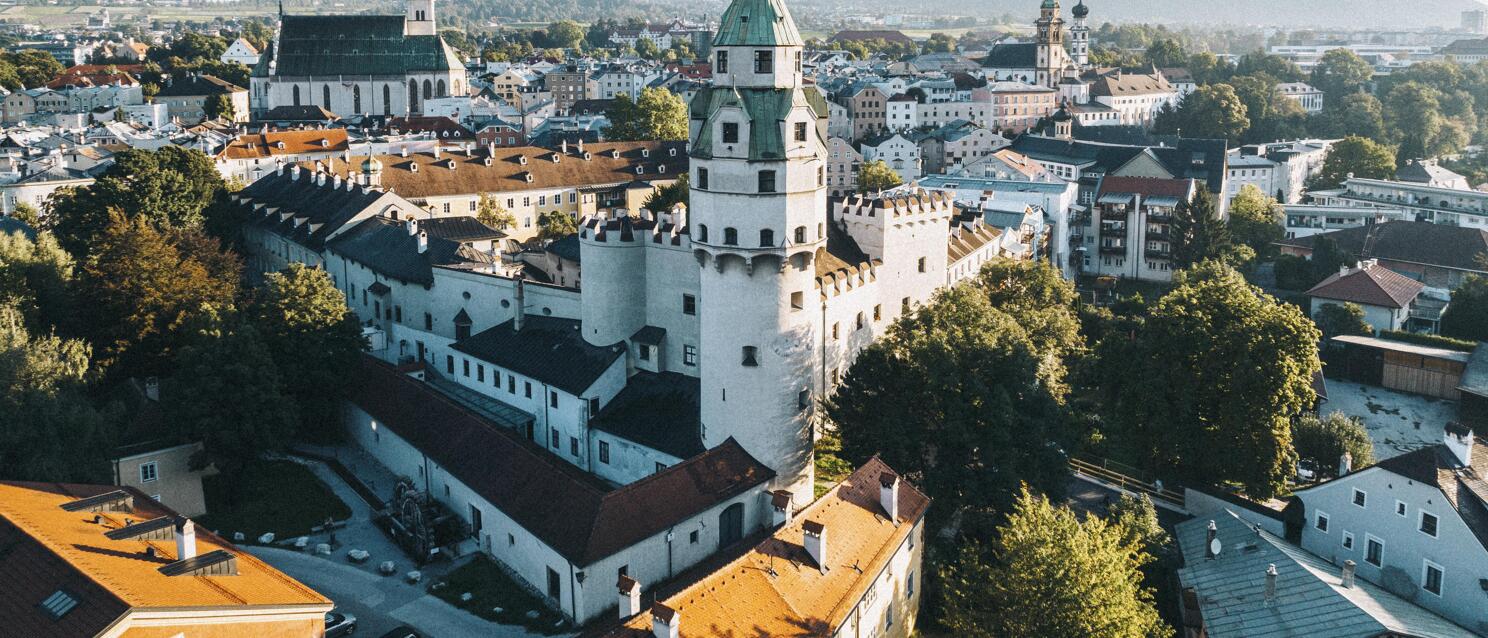 Aerial view of Hall in Tirol with white Hasegg Castle, old town and mountains in background.