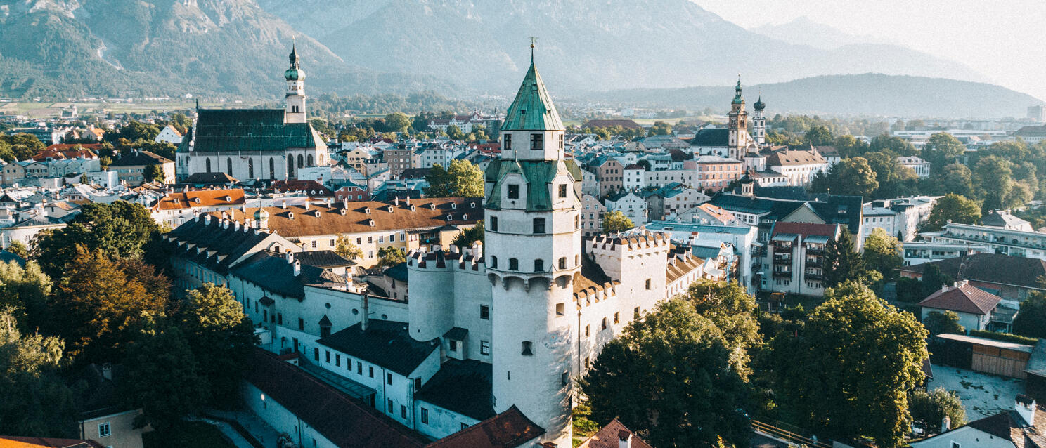 Aerial view of Hall in Tirol with white Hasegg Castle, old town and mountains in background.