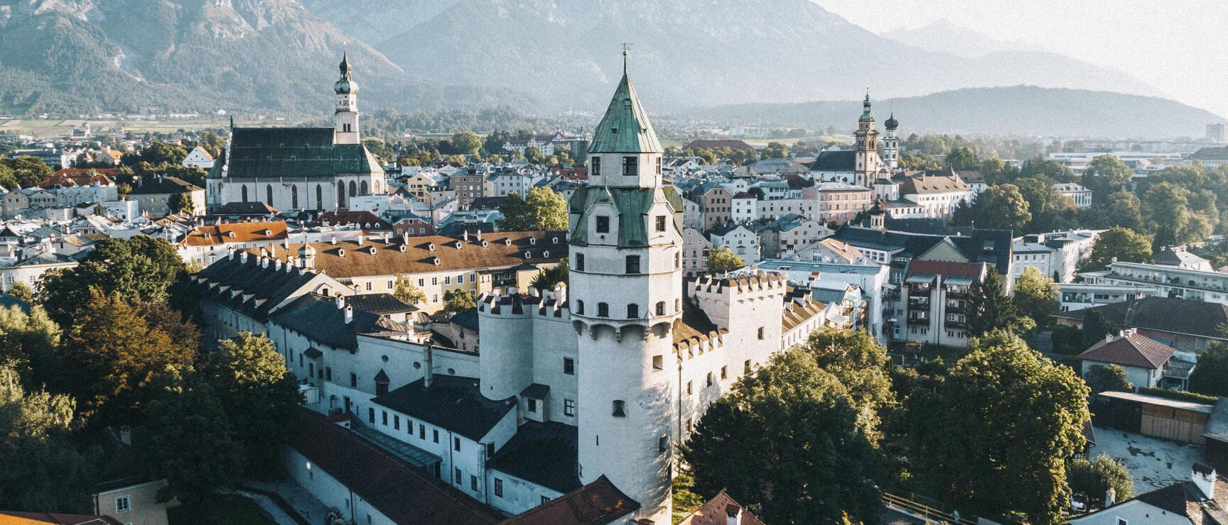 Aerial view of Hall in Tirol with white Hasegg Castle, old town and mountains in background.