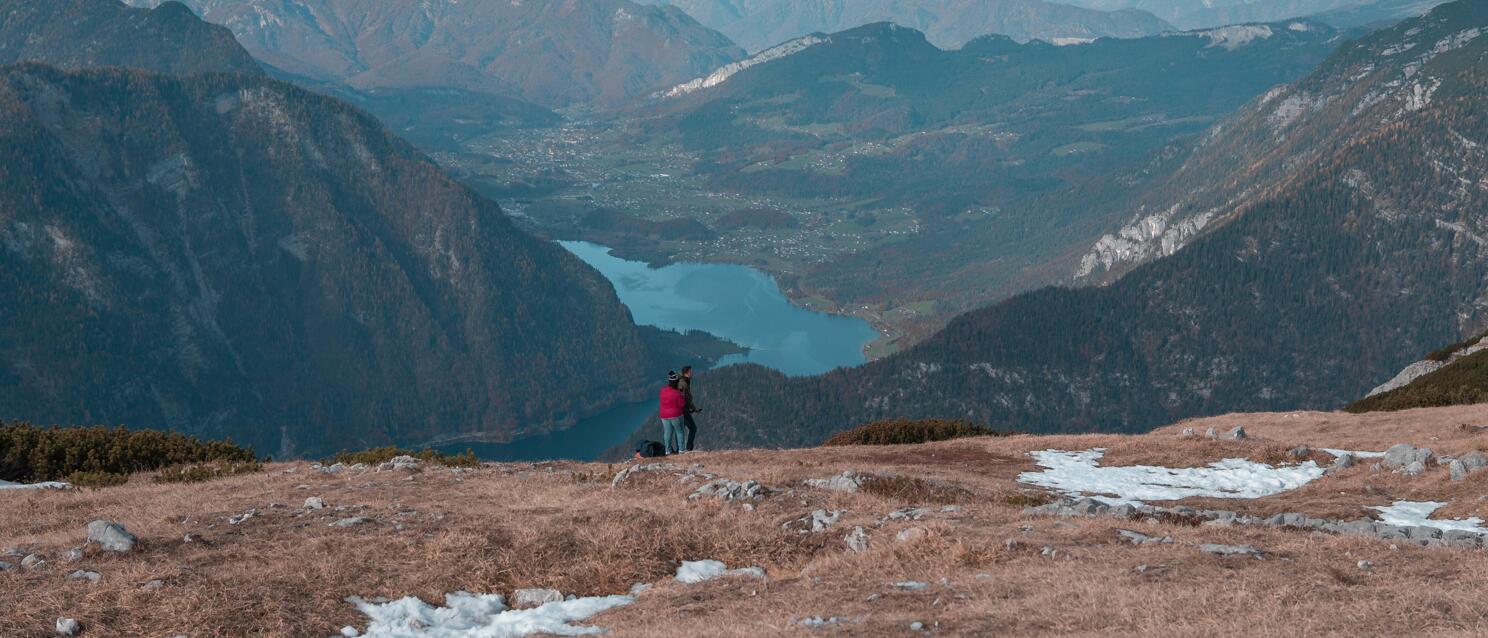 Two people on a mountain summit gazing at Hallstatt Lake and vast mountain ranges in the Salzkammergut.