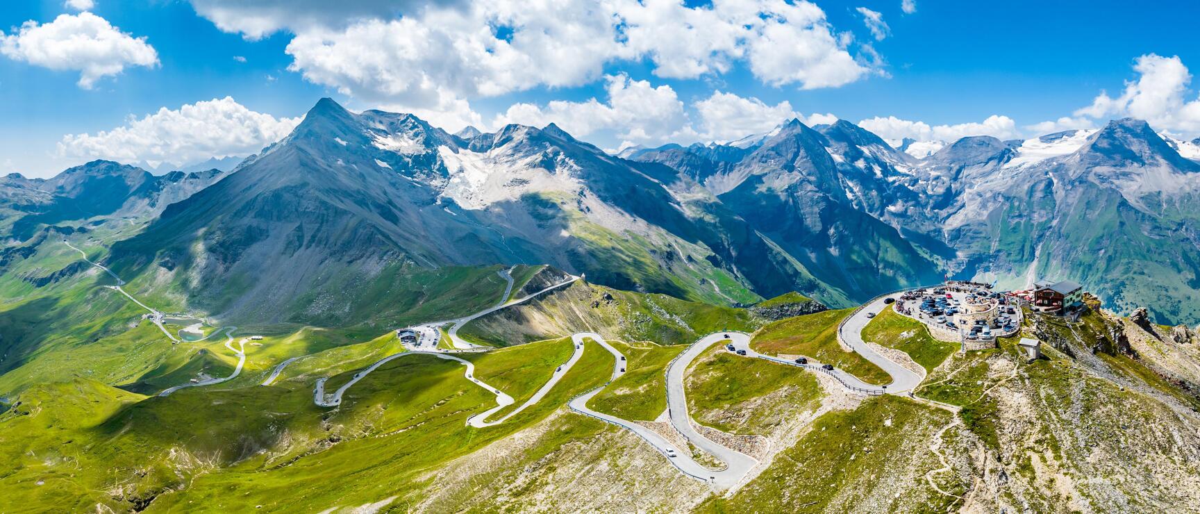 Serpentine road of Großglockner High Alpine Road with snow-covered peaks and car park on the right.
