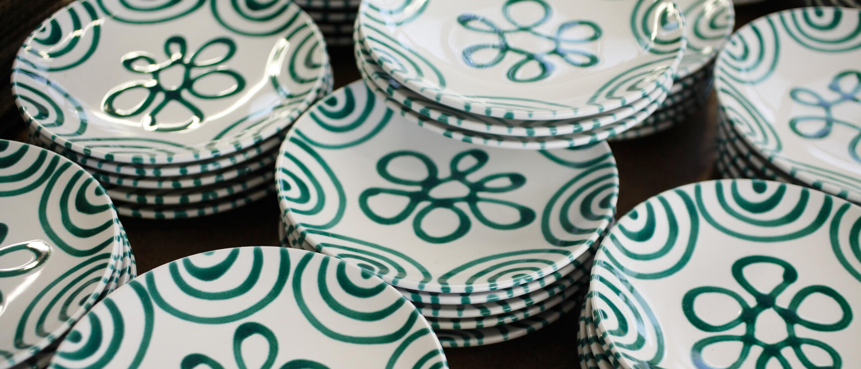 Multiple stacked white ceramic plates with green floral and spiral pattern.