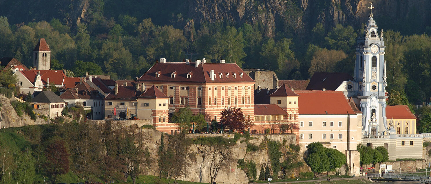 View across the Danube to Dürnstein with blue abbey tower and red tile roofs, rock face in background.