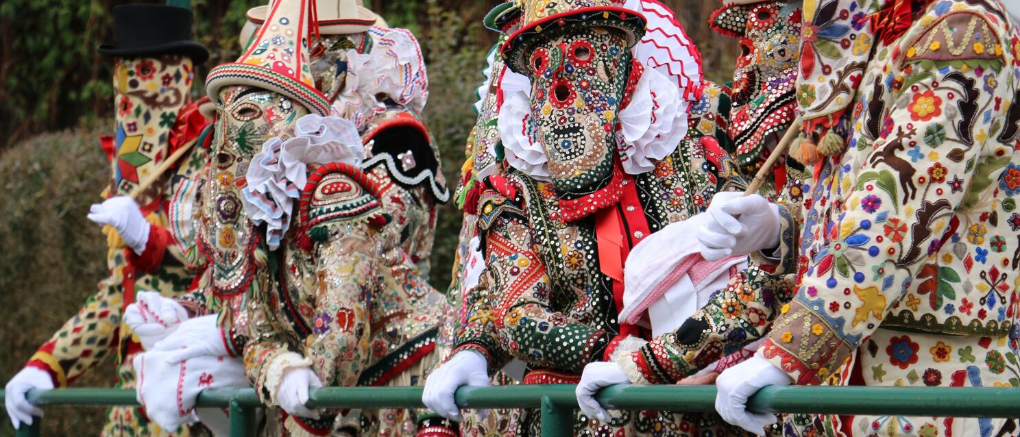 Several carnival figures in colorful embroidered costumes and masks with top hats at the carnival parade.