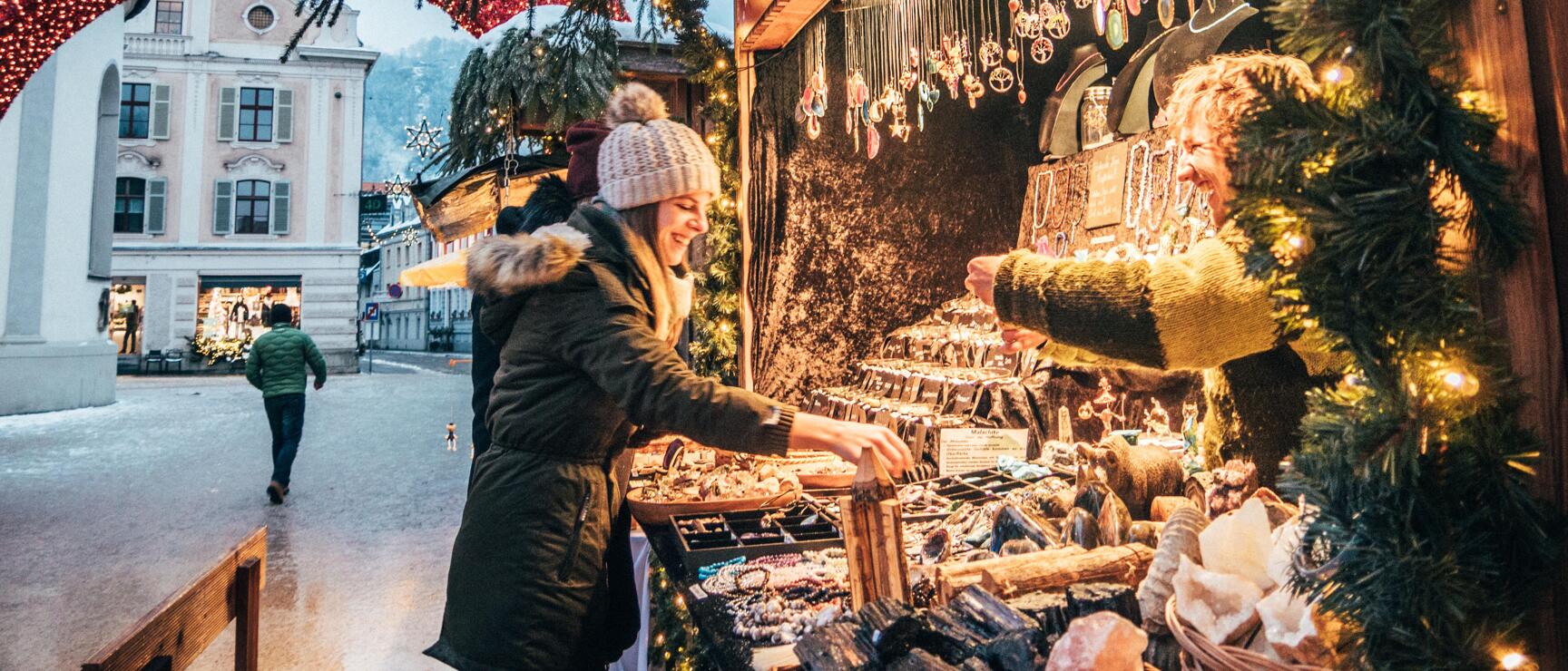 Woman in wool hat at a jewellery stand on a Christmas market in Bregenz, red light arch in the background.