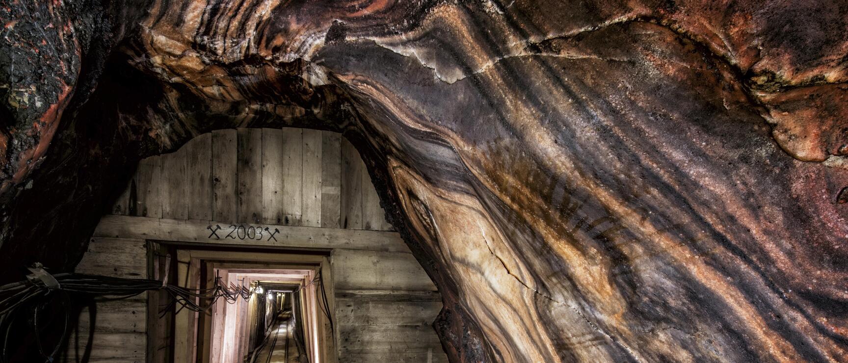 Wooden-clad tunnel in a salt mine with patterned salt wall, '2003' inscription above the passage.