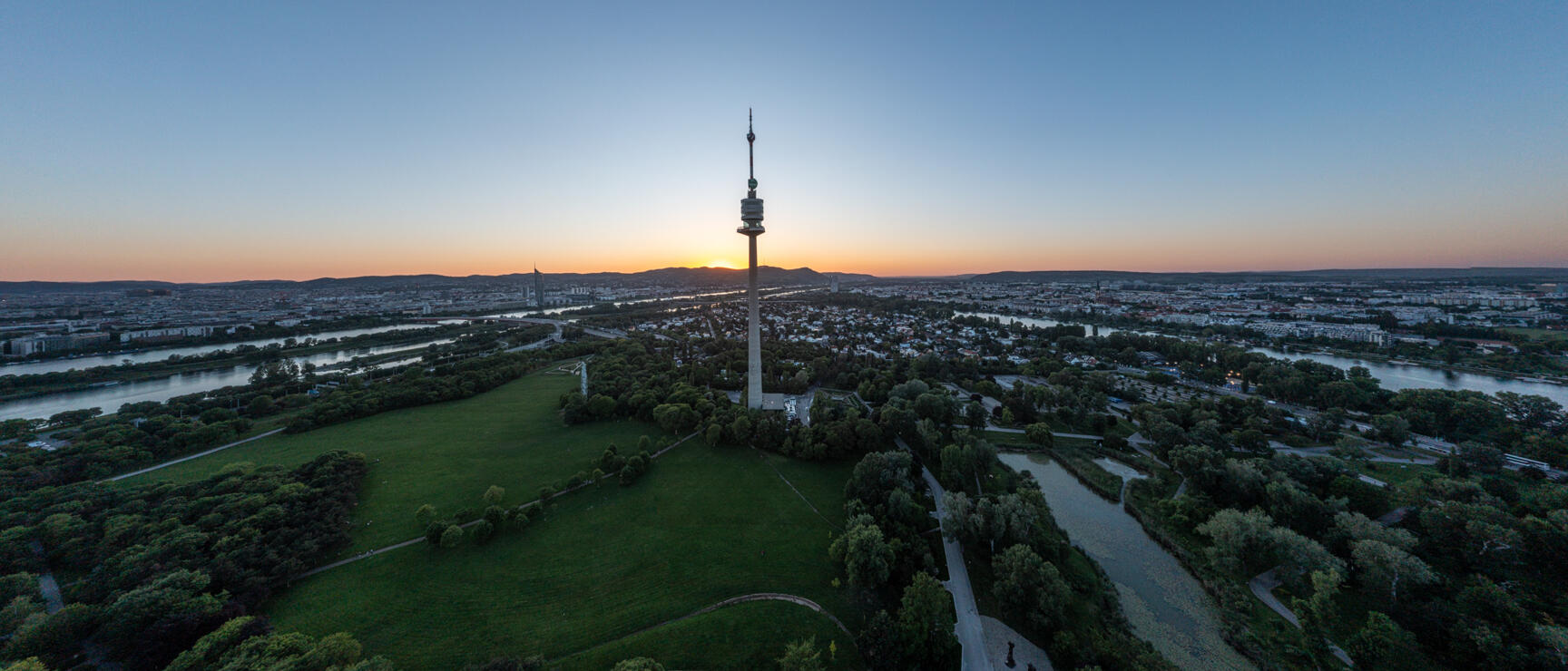 Aerial view of Danube Tower in Danube Park Vienna at sunset, Danube river and city skyline in background.