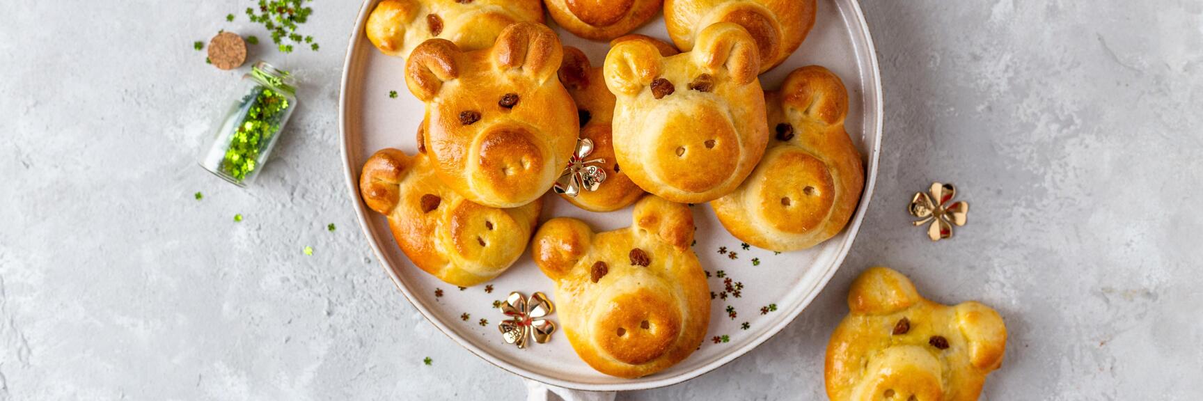 Golden-brown yeast rolls shaped like piglets on a plate, decorated with golden clover and green sprinkles