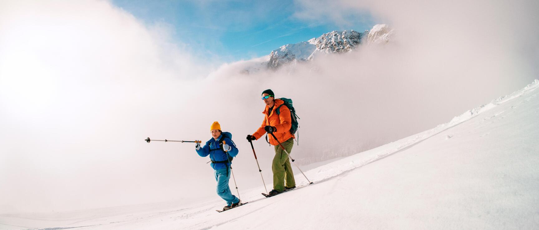 Zwei Schneeschuhwandernde bewegen sich durch eine weitläufige, verschneite Winterlandschaft in den österreichischen Alpen. Die sanften Wolken, die unberührten Schneeflächen und die ruhige Atmosphäre vermitteln Naturverbundenheit, Freiheit und das besondere Erlebnis gemeinsamer Wintertouren in Österreich.