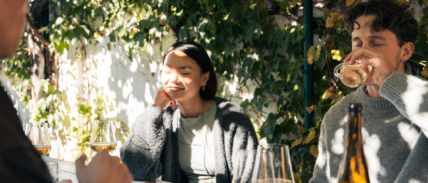 Two people at an outdoor table with wine glasses and bottle, vineyards in the background.