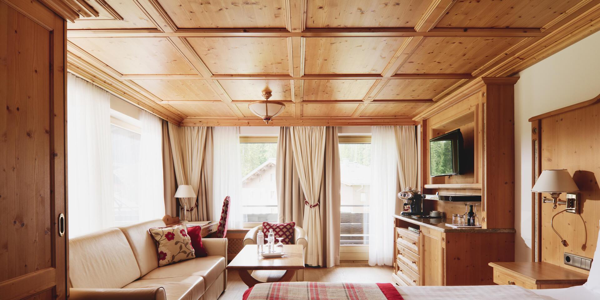 Hotel room with wooden ceiling, checked bedspread, sofa with cushions and wooden furniture.