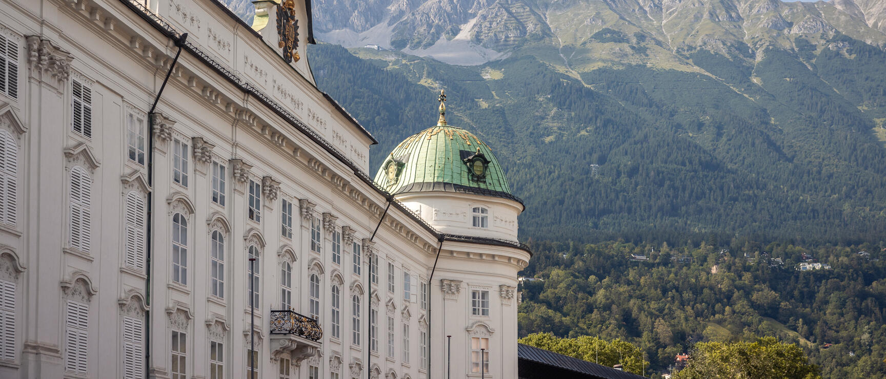 Hofburg Innsbruck with green dome, forested Nordkette mountains behind under blue sky