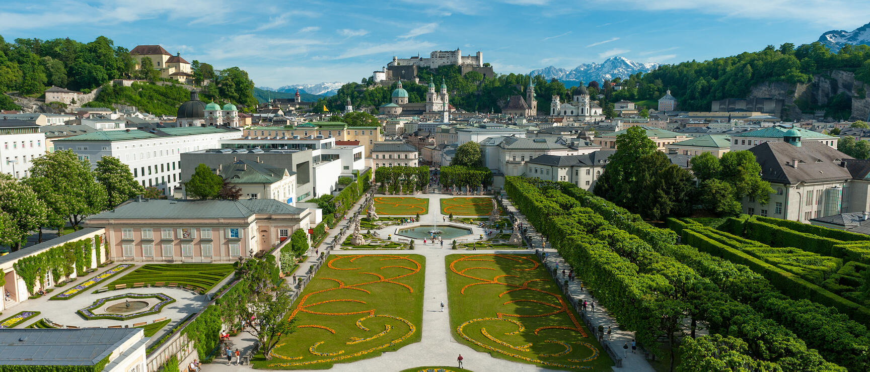Mirabell Garden Salzburg with flower beds, fountains, Hohensalzburg Fortress and Alps in the background.