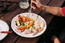 Brettljause board with cold cuts, cheese, pickles, peppers and onions on a plate, hand with fork reaching for food.