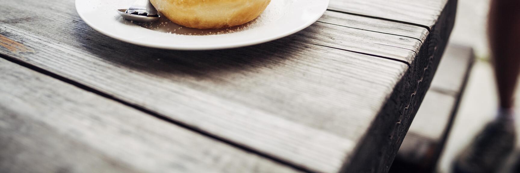 Yeast dumplings with plum compote and icing sugar on white plate, spoon beside, rustic wooden table