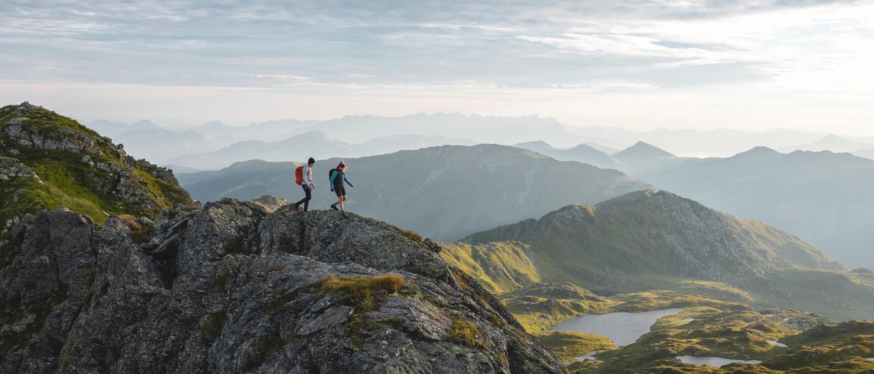 Two hikers on a rocky ridge with a view of mountain lakes and the vast mountain landscape of the Kitzbühel Alps in the Brixental valley