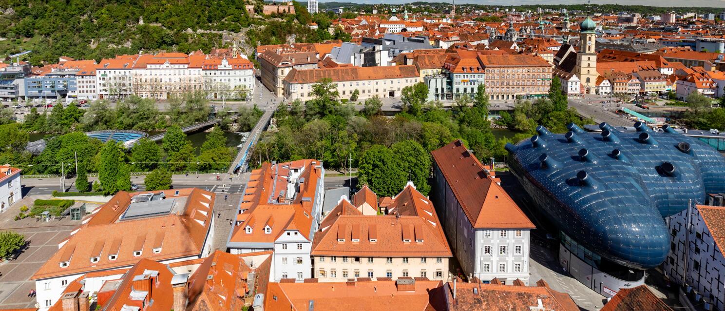 Aerial view of Graz with Kunsthaus, clock tower on Schlossberg and red tiled roofs of the old town.