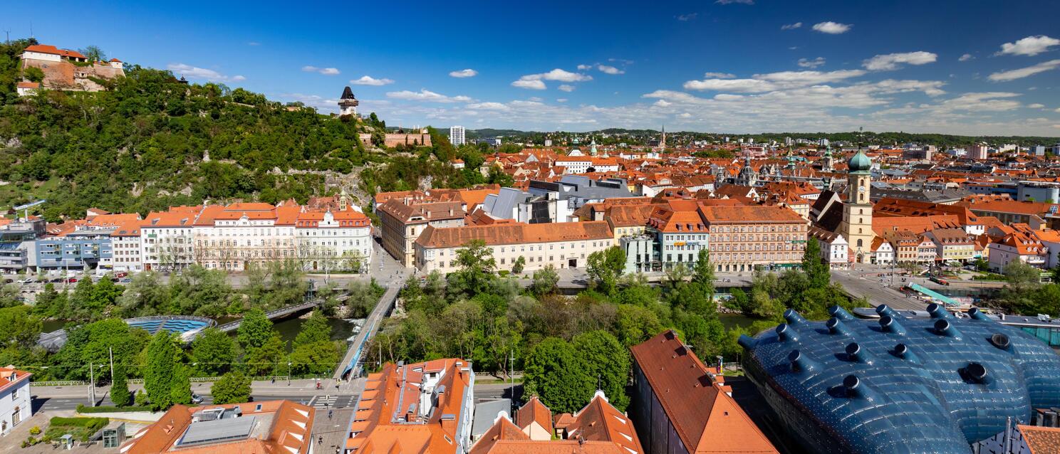 Aerial view of Graz with Kunsthaus, clock tower on Schlossberg and red tiled roofs of the old town.