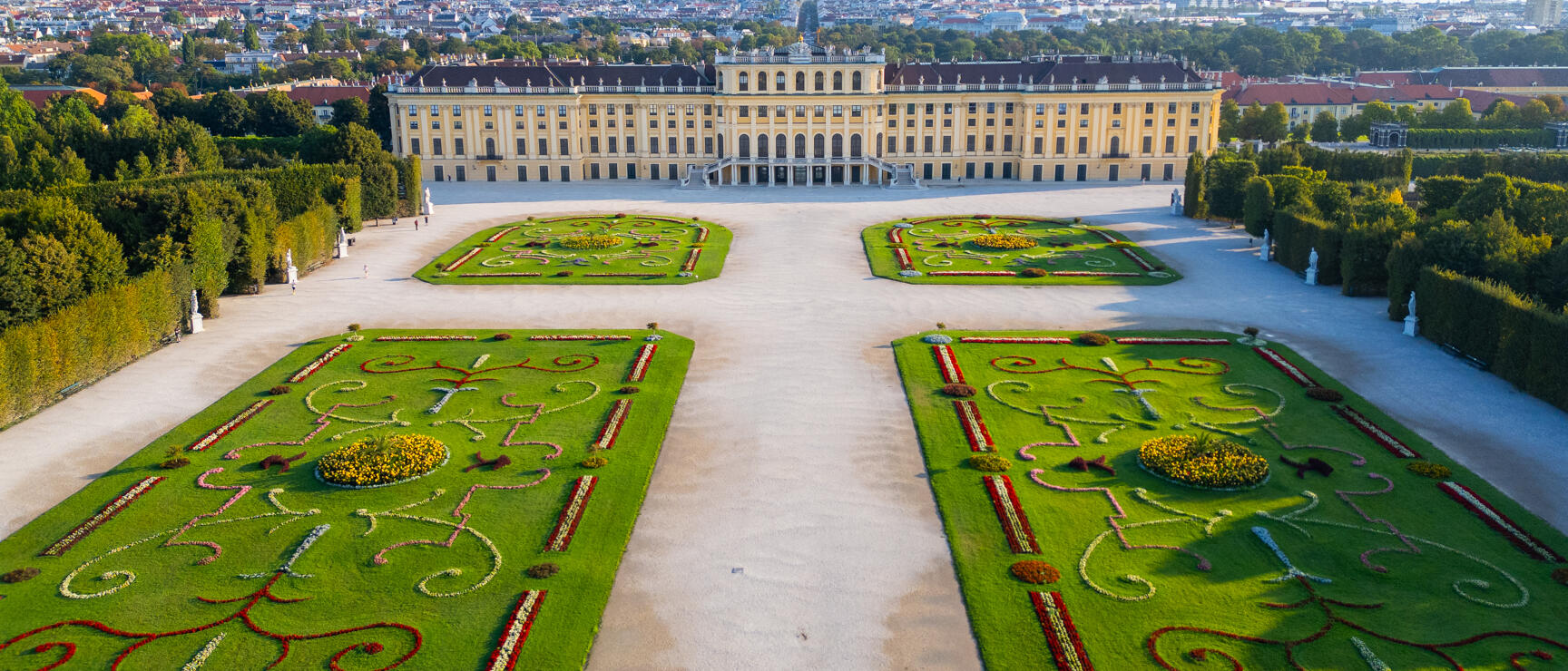 Schönbrunn Palace with Baroque garden parterres, Vienna in background, aerial view with blue sky.
