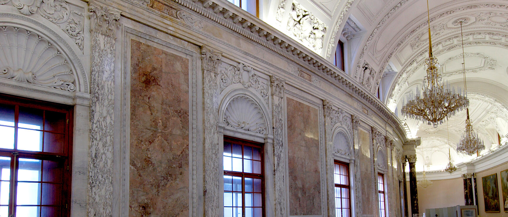 Magnificent marble hall with crystal chandeliers, stucco decorations and curved staircase in a Viennese palace.