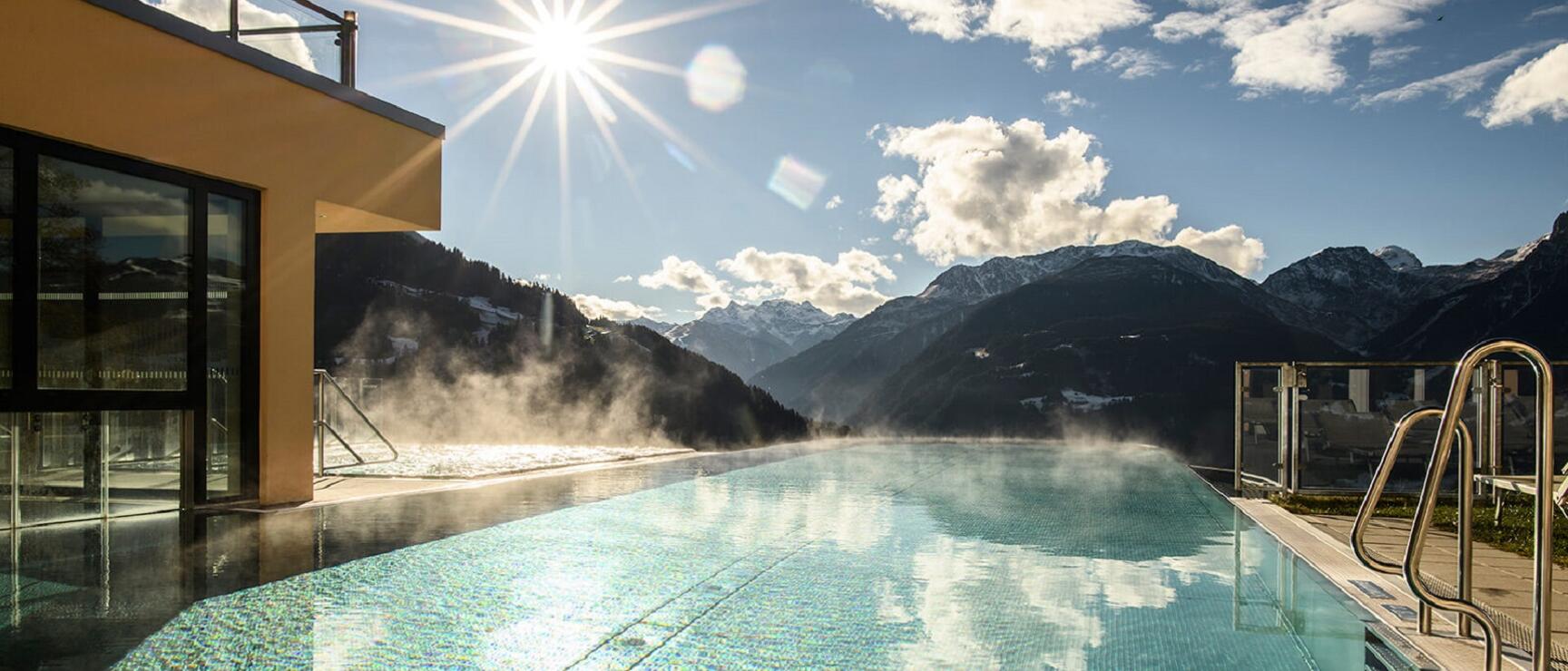 Steaming infinity pool with snow-capped mountains in sunny weather