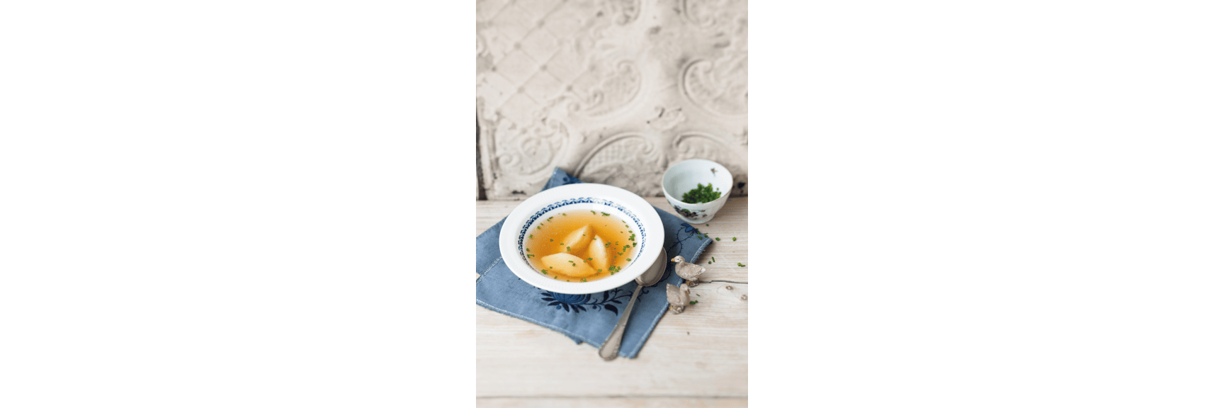 Semolina soup with chives in a blue and white bowl, spoon and small dish of chives nearby.