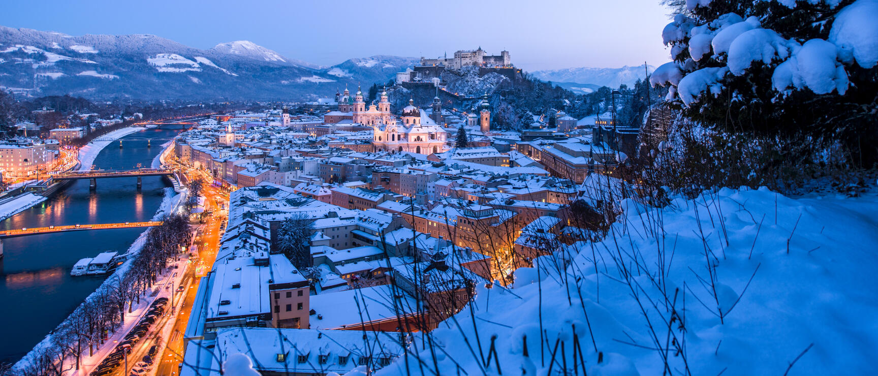 Winter view of Salzburg at dusk, snow-covered old town with cathedral, Hohensalzburg Fortress, Salzach River.
