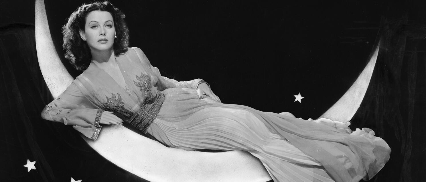 Woman in long dress lying on crescent moon prop with stars in background, black and white photo