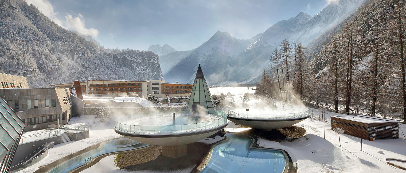 Aqua Dome Längenfeld thermal bath in winter: steaming outdoor pools with snow-capped mountains in background.