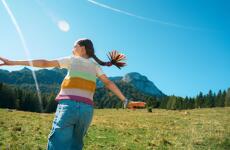Girl with outstretched arms on alpine meadow with mountain landscape and blue sky in background.